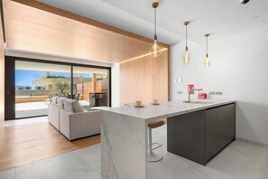 A modern kitchen with a marble island, pendant lights, and a view to an outdoor seating area. - Luma (Fuengirola)