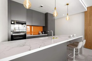 A modern kitchen with a marble countertop, stainless steel appliances, and pendant lighting. - Luma (Fuengirola)