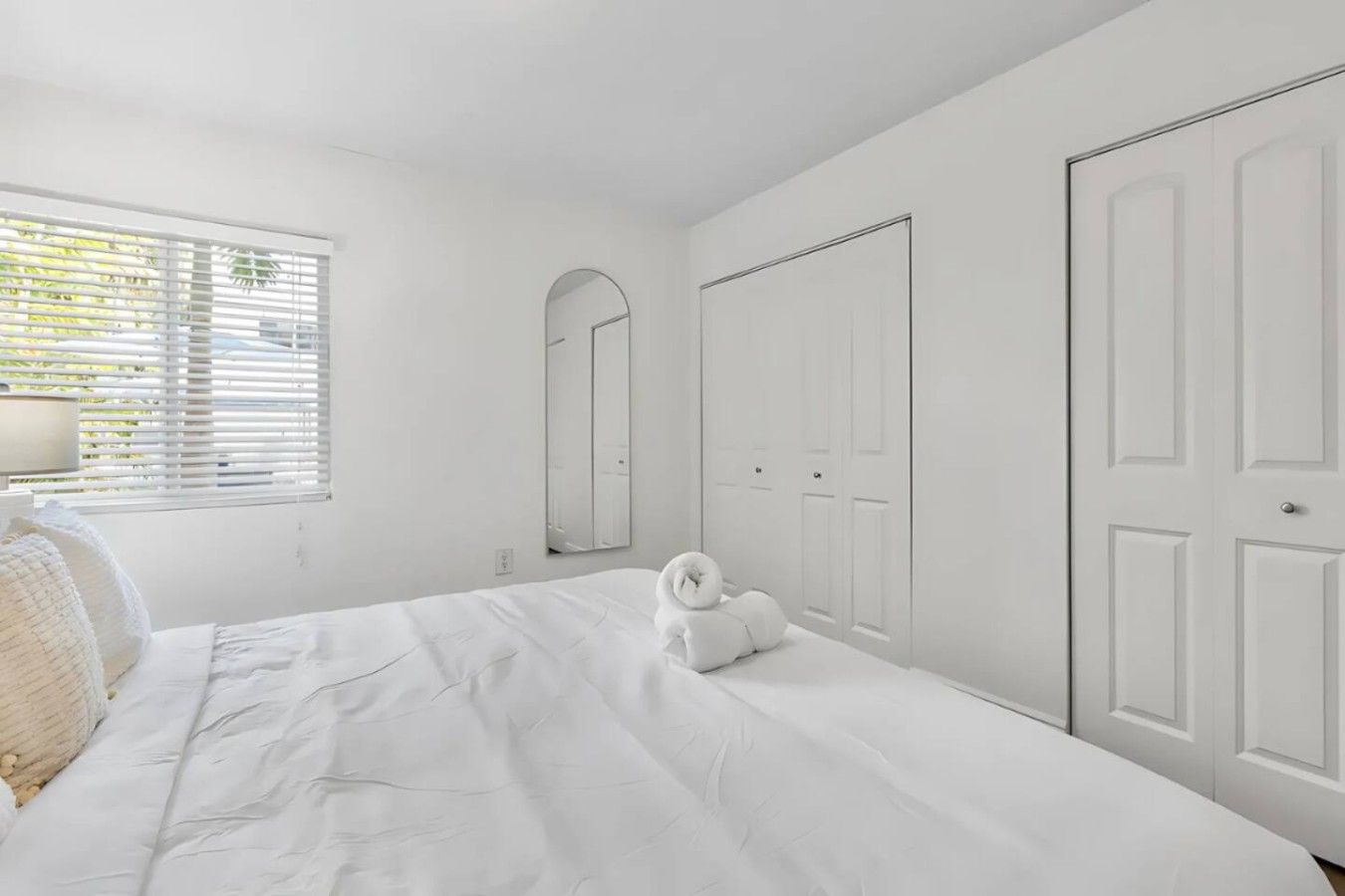 Une chambre à coucher comprenant un lit, une table de chevet, une lampe, un miroir et une armoire.