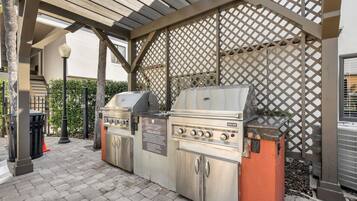 Een terras met een barbecue, een pergola erboven, een afvalbak en een straatlamp.
