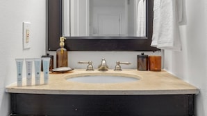 A bathroom with a beige sink, a large mirror, and toiletries including a shampoo bottle and a soap dispenser. - Bayshore Retreat | Pool, Gym & Free Parking (Tampa)