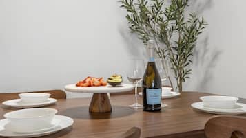 A dining table with a white plate of strawberries and avocado, a bottle of wine, and empty wine glasses.