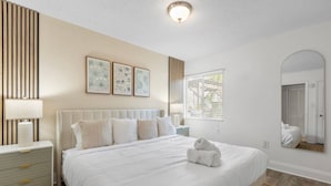 A bedroom with a large bed, bedside tables, a mirror, and wall art. - Bayshore Retreat | Pool, Gym & Free Parking (Tampa)