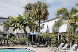 A pool area with lounge chairs, a table, and umbrellas. - Bayshore Retreat | Pool, Gym & Free Parking (Tampa)