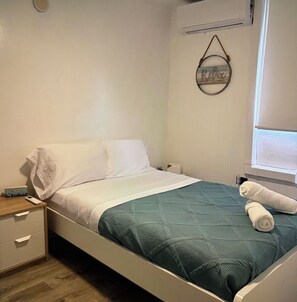 A single bed with a teal bedspread, a white pillow, and a wall-mounted towel rack with a towel. - 3-Bed. Modern loft with gated parking near SJU (San Juan)