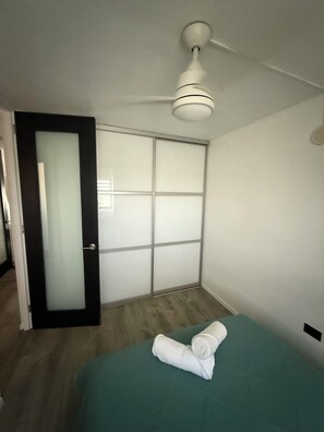 Ein Zimmer mit einem Bett, einem Deckenventilator, einer Schiebetür und Holzboden.