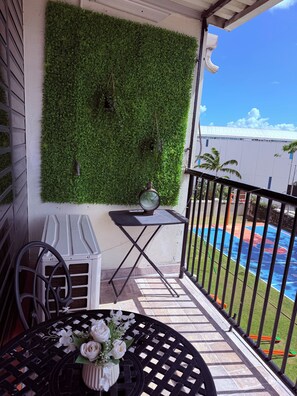 A balcony with a green wall, a small table with a vase of flowers, and a view of a swimming pool. - 3-Bed. Modern loft with gated parking near SJU (San Juan)
