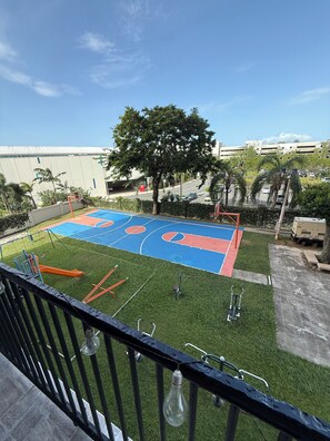 A basketball court with a blue and red surface, surrounded by green grass and trees. - 3-Bed. Modern loft with gated parking near SJU (San Juan)