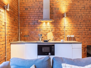 A compact kitchen with a brick wall, a built-in microwave, and a hanging pot rack. - Student Only Ashton House (Manchester)