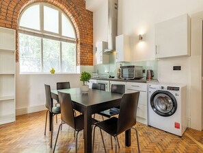 A compact kitchen with a brick wall, white cabinets, a microwave, a toaster, and a washing machine. - Student Only Ashton House (Manchester)