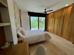 A bedroom with a bed, a desk, a chair, a ceiling fan, and a view of greenery outside. - Villa Velas | Private Pool, Hot Tub & Rooftop | Gated Cabo Bello (Cabo San Lucas)