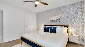 Quarto com cama, ventoinha no teto, mesa de cabeceira e parede estampada.