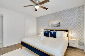 Quarto com cama, ventoinha no teto, mesa de cabeceira e parede estampada.