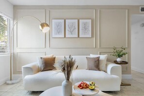Un saló modern amb un sofà blanc, coixinets decoratius, una làmpada de peu i impressores enmarcades amb motius botànics a la paret.