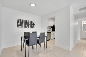 Een moderne eethoek met een tafel en stoelen, een keuken op de achtergrond en een gang naar een andere kamer.