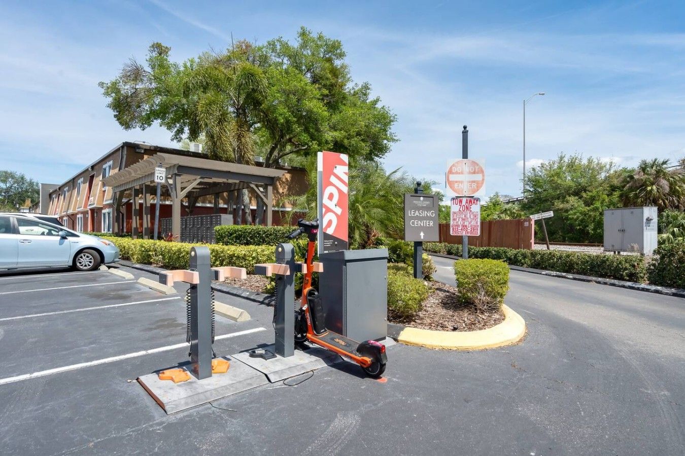 A parking area with a sign for a leasing center, a tow-away zone sign, and a building with a covered entrance.