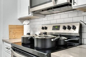 Una cocina con estufa de acero inoxidable, dos ollas encima y un reloj digital que marca las doce.