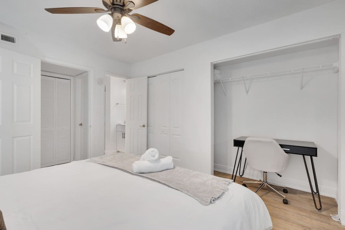 Ein Schlafzimmer mit Bett, Schreibtisch, Stuhl, Deckenventilator und begehbarem Kleiderschrank.