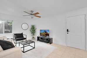 A living room with a sofa, armchair, coffee table, TV, and a ceiling fan. - South Tampa Getaway | FREE Pool, Gym & Parking (Tampa)