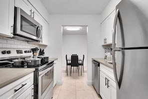 A modern kitchen with stainless steel appliances, a dining area with a table and chairs, and a hallway leading to another room. - South Tampa Getaway | FREE Pool, Gym & Parking (Tampa)