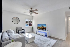 Uma sala de estar moderna com sofá, mesa de centro, televisão e ventilador de teto.