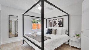A bedroom with a four-poster bed, a bedside table, a mirror, and abstract wall art. - South Tampa Coastal Stay | Pool & Free Parking (Tampa)