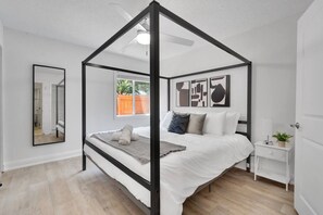 Ein Schlafzimmer mit Himmelbett, Nachttisch, Spiegel und abstrakten Wandbildern.