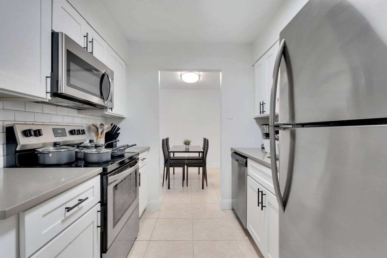 A narrow kitchen with stainless steel appliances, a dining area with a table and chairs, and a view into the dining room.