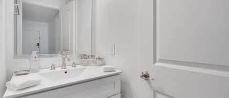 Un baño con tocador blanco, espejo y puerta.