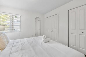 A bedroom with a bed, a bedside table, a lamp, a mirror, and a wardrobe. - Near the Shore | Pool, Gym & Free Parking (Tampa)