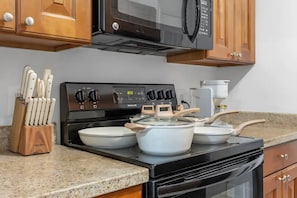 A kitchen with a black stove, wooden cabinets, and a granite countertop. - Near the Shore | Pool, Gym & Free Parking (Tampa)