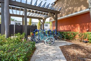A covered bike parking area with multiple bicycles, a paved walkway, and a building with a red exterior wall. - Near the Shore | Pool, Gym & Free Parking (Tampa)
