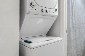A front-loading washing machine with a control panel, a door, and a wall-mounted vent. - Near the Shore | Pool, Gym & Free Parking (Tampa)