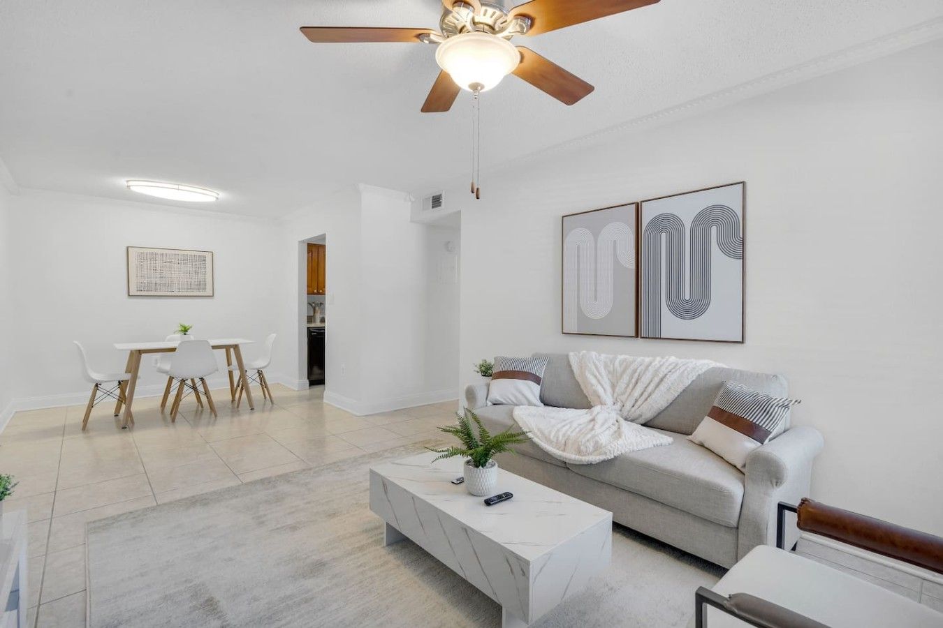 Uma sala de estar moderna com ventilador de teto, um espaço de jantar com mesa e cadeiras, e um sofá com manta.