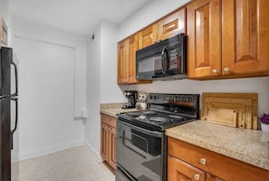 A kitchen with wooden cabinets, a black microwave, a stove, and a countertop. - Palma Ceia Retreat | Pool, Gym & Free Parking (Tampa)