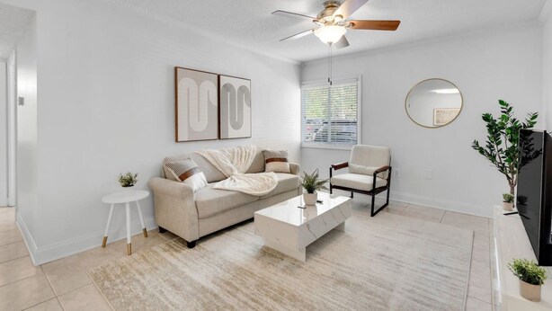 A modern living room with a sofa, coffee table, armchair, ceiling fan, and a television. - Bayshore Bliss | Pool, Gym & Free Parking (Tampa)
