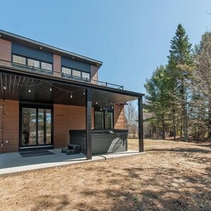 A modern two-story house with a covered patio area and a hot tub.