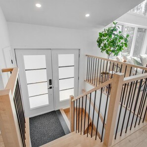 A modern interior with a staircase, a door with frosted glass panels, and a potted plant. - Chalet le ZÖR | On the Lakeshore (Saint-Alphonse-Rodriguez)