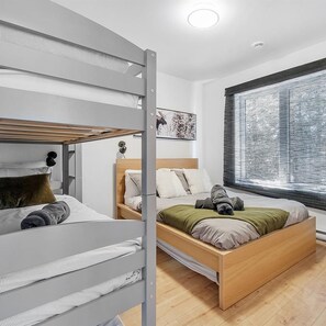 A bedroom with a bunk bed, a single bed, and a window with blinds. - Vrbo Property (Saint-Alphonse-Rodriguez)