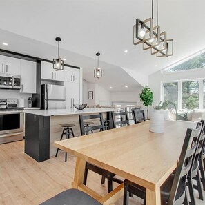 A modern kitchen with a central island, stainless steel appliances, and a dining area with a wooden table and chairs. - Vrbo Property (Saint-Alphonse-Rodriguez)