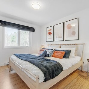 Una camera da letto moderna con un letto di legno, biancheria bianca e una grande finestra vista alberi.