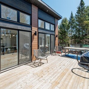 A modern house with a deck, large sliding glass doors, and outdoor furniture. - Vrbo Property (Saint-Alphonse-Rodriguez)