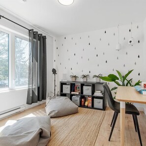 A modern living room with a large window, a dining area with a table and chairs, a bookshelf, and a floor lamp.