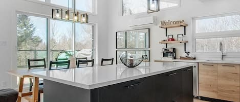 A modern kitchen with a large island, pendant lighting, and a 'Welcome' sign above the sink.
