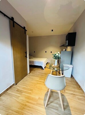 Una habitación pequeña con una cama, una mesita con una silla, televisión y una puerta corredera.