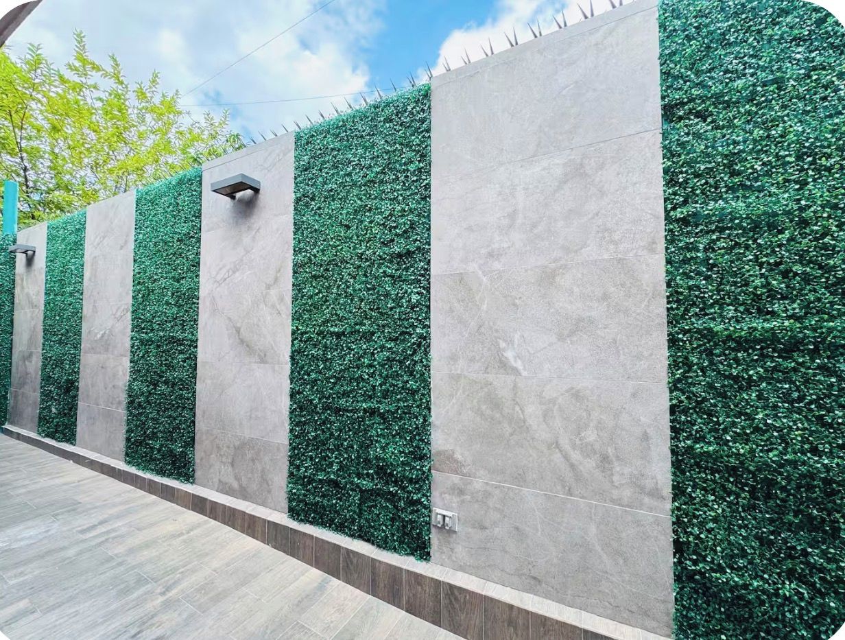 A wall with alternating vertical panels of artificial green foliage and smooth grey tiles.