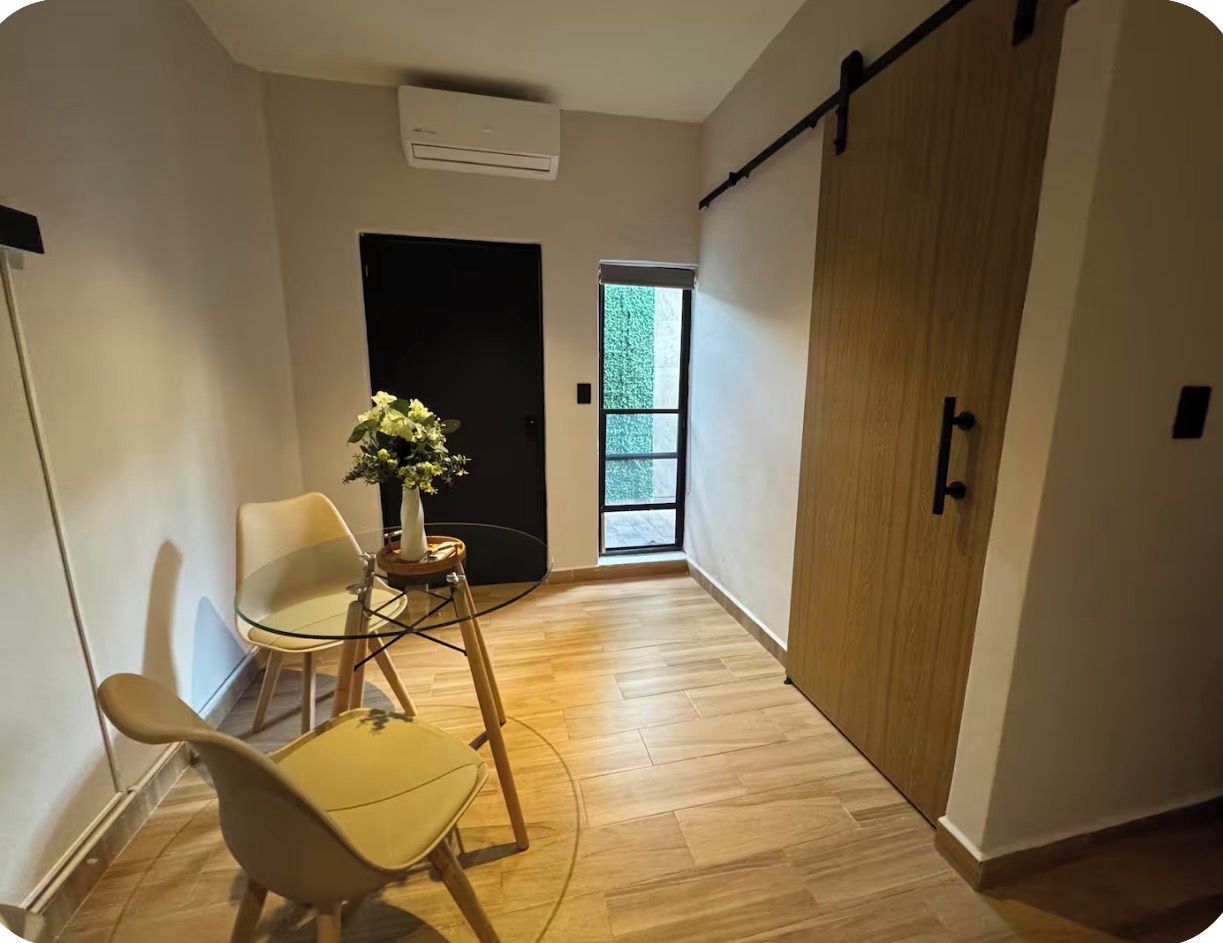 A hallway with a sliding door, a small table with a plant, two chairs, and a window with a view of greenery.