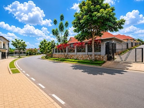 A residential street with houses, a curved road, and a clear sky. - Secure 4BR Home Near City Center (Kigali)