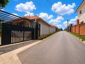 A residential street with houses on both sides, a gated entrance, and a clear sky.