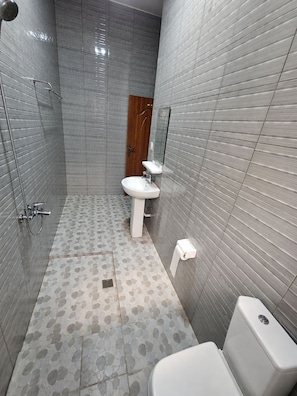 Een badkamer met een douche, wastafel, toilet en een spiegel.